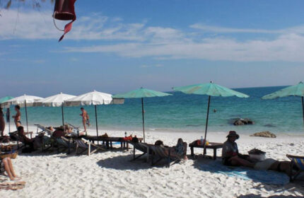 Tok Little Hut, Koh Samet beachfront. Beach scene with people relaxing under umbrellas. Cheap gay hotel, perfect for gay travel.