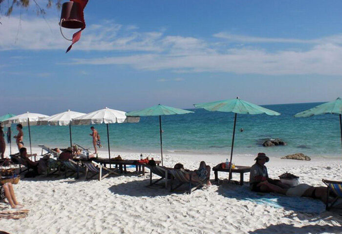 Tok Little Hut, Koh Samet beachfront. Beach scene with people relaxing under umbrellas. Cheap gay hotel, perfect for gay travel.