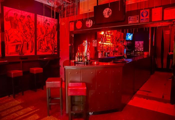 Interior of Tom's Cruising Bar, a gay cruise club in Gran Canaria. Red lighting, bar stools, provocative art, and a fully stocked bar.
