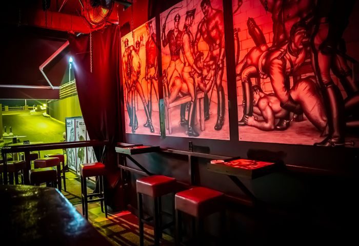 Interior of Tom's Cruising Bar, a gay cruise club in Gran Canaria. Red lighting, bar stools, and suggestive artwork on the wall. Gay travel.