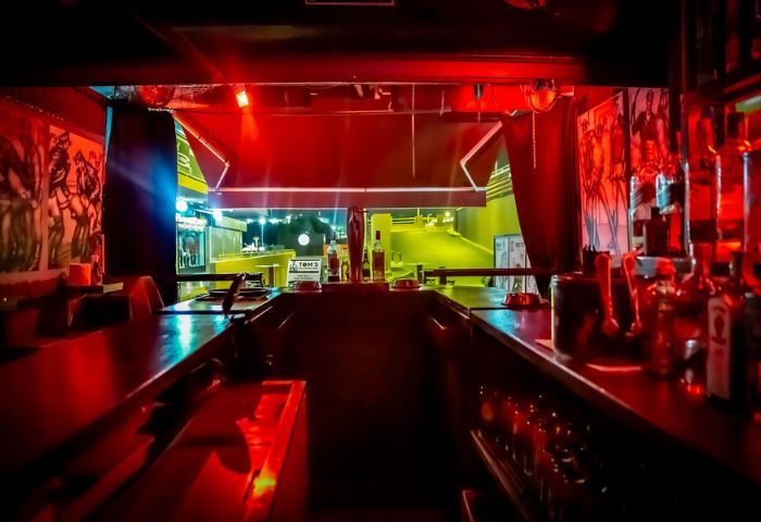 Tom's Cruising Bar, a gay cruise club in Gran Canaria. Interior view with red lighting, bar counter, bottles, and a glimpse of the outside street.