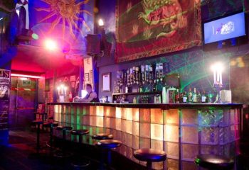 Tom's Leather Bar: A gay bar in Mexico with a lively party atmosphere. Drinks line the bar, stools in front. Sun and dragon art adorn the walls.