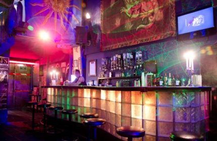Tom's Leather Bar: A gay bar in Mexico with a lively party atmosphere. Drinks line the bar, stools in front. Sun and dragon art adorn the walls.
