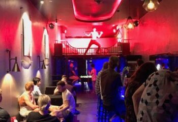 Toolbox Bar Phnom Penh: Gay bar interior with patrons & dancer on stage. Red lighting, pool table, & unique decor. Gay travel advice.