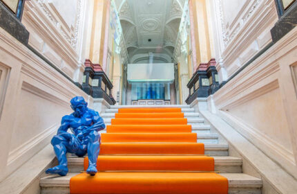 meetme23, top party hostel in Prague's gayborhood. Blue sculpture sits on orange-carpeted stairs in the grand lobby of this gay-friendly hotel.