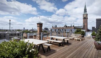 Hotel Danmark by Brøchner Hotels rooftop view in Copenhagen's Vesterbro gayborhood. Design hotel with tables, benches, and city skyline.