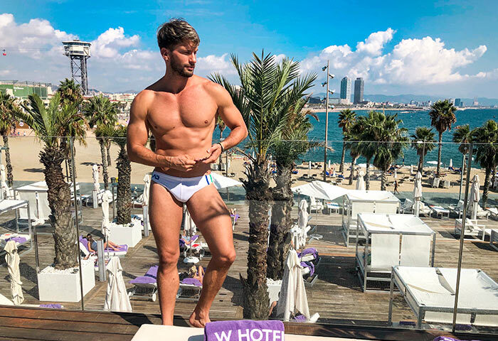 Gay-friendly W Barcelona hotel view. Fit man on the terrace with beach, palm trees, and city skyline. Top choice for gay travel in Barcelona.