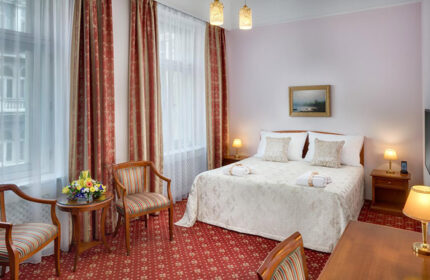 Boutique Hotel Seven Days room in Prague's gayborhood Vinohrady. Elegant interior, double bed, red carpet, chairs, and warm lighting.