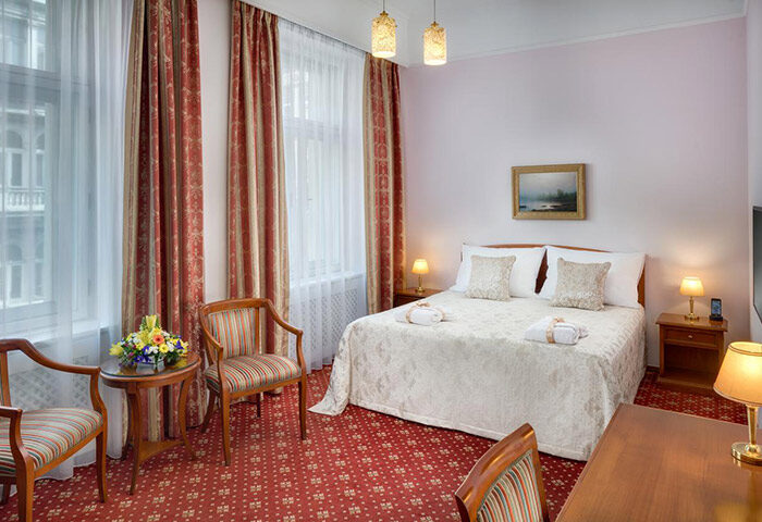 Boutique Hotel Seven Days room in Prague's gayborhood Vinohrady. Elegant interior, double bed, red carpet, chairs, and warm lighting.
