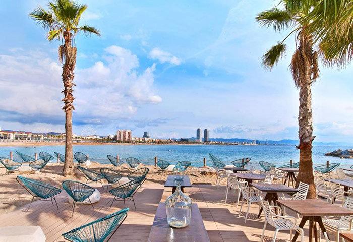 W Barcelona beachfront hotel view. Beachside seating, palm trees, & ocean views. Top gay-friendly hotel in Barcelona.