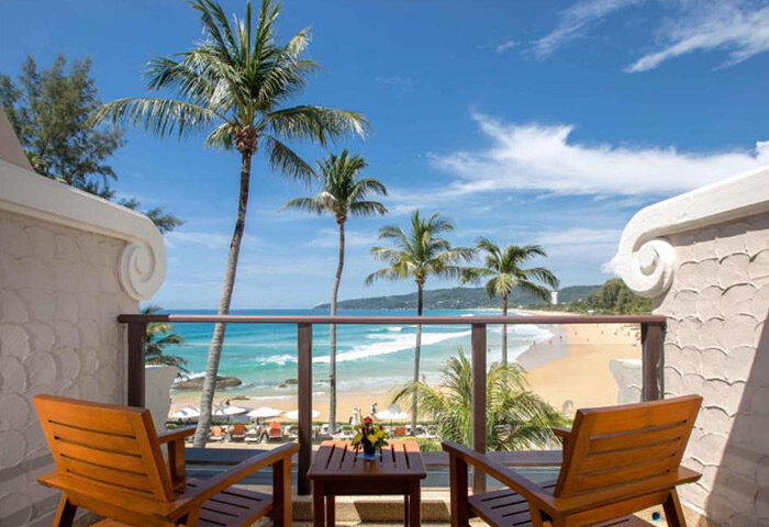 Beyond Resort Karon, Phuket adults-only honeymoon hotel view. Balcony with chairs overlooking Karon Beach, palm trees, and turquoise sea.