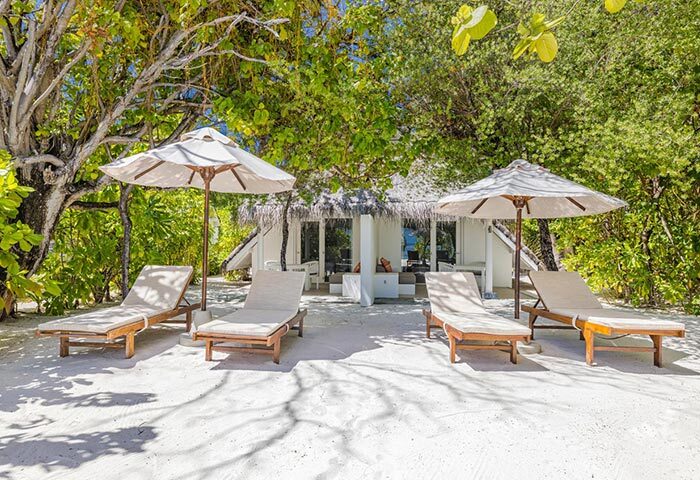 Beachfront at LUX* South Ari Atoll, Maldives. Gay resort with sunbeds and umbrellas for four people on white sand. Tropical luxury.