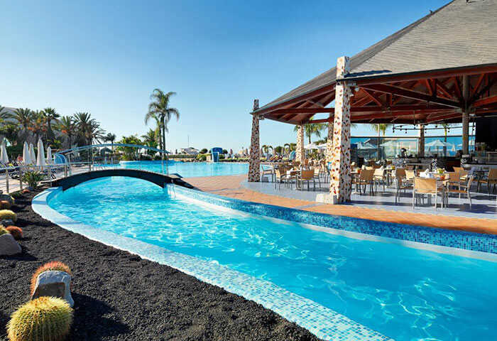 H10 Playa Meloneras Palace pool area in Gran Canaria. Top beachfront luxury gay hotel with bar, bridge, and clear blue water.