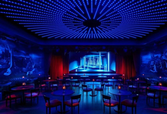 The Times Square EDITION's Paradise Club. A design hotel in Hell's Kitchen gayborhood. Blue lights, stage, tables, chairs, red curtains.
