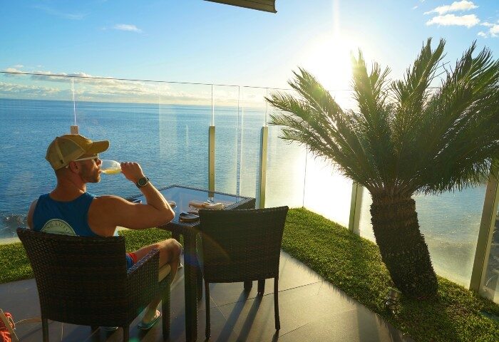 Gay man enjoying wine at Saccharum Hotel, Madeira. Ocean view, palm tree, sunny day. Top gay beach hotel on Instagram and TikTok. Portugal travel.
