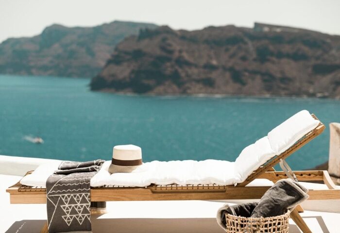 Armenaki Santorini gay honeymoon hotel. Beach view with sunbed and hat. Top gay travel destination. Relaxing beach hotels in Santorini.