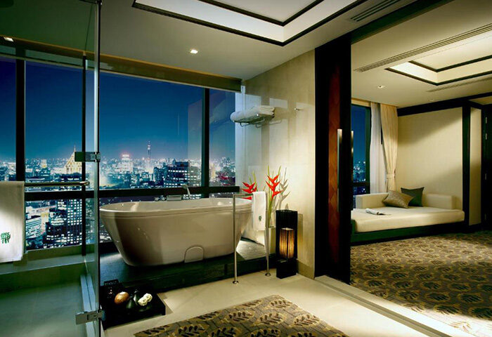 Banyan Tree Bangkok luxury hotel bathroom view. Top gay honeymoon choice in Bangkok. Bathtub overlooking the city skyline at night.