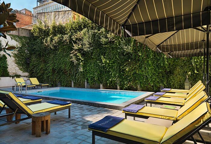 H10 Metropolitan Hotel pool in Barcelona's Eixample. Top gay hotel with sun loungers, umbrellas, and lush greenery for a relaxing stay.