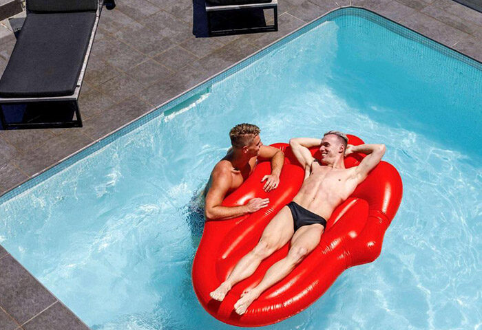 Gay Pullman Sydney Hyde Park hotel pool scene. Two men relax on a red lips floatie in the water. Top gay hotel in Sydney's gay area.