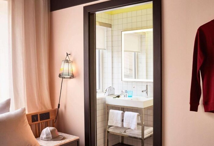 Mama Shelter London Shoreditch hotel room view. A bathroom with a sink, mirror, and towels is visible. Top gay hotels for solo travelers.