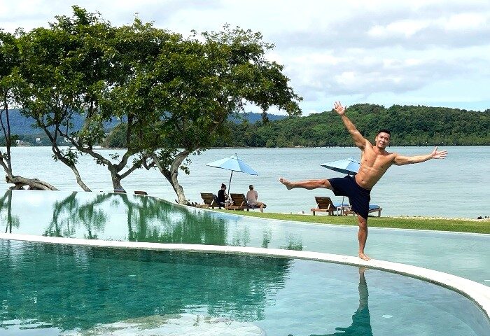 Gay luxury travel: Man balances on pool edge at The Naka Island, a Luxury Collection Resort & Spa, Phuket. Tropical private island hotel.