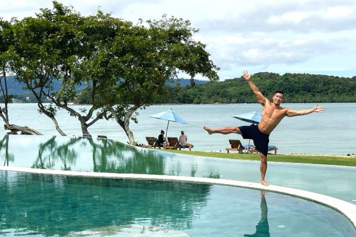 Gay luxury travel: Man balances on pool edge at The Naka Island, a Luxury Collection Resort & Spa, Phuket. Tropical private island hotel.