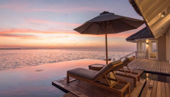 Gay LUX* South Ari Atoll, Maldives over-the-water beach pool villa. Sunset view from deck chairs, perfect for gay couples' travel.