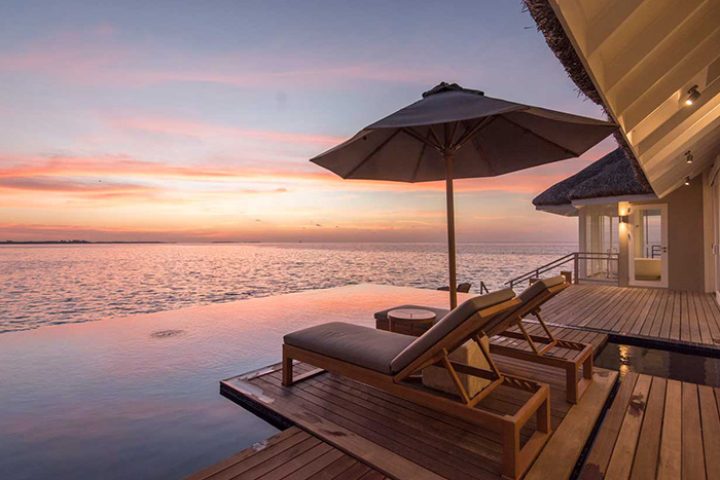 Gay LUX* South Ari Atoll, Maldives over-the-water beach pool villa. Sunset view from deck chairs, perfect for gay couples' travel.