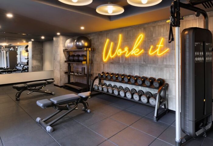 Le Meridien Melbourne gym. Wellness hotel's fitness center in Collingwood features weights, benches, and a Work It neon sign. Top gay hotel.