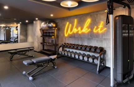 Le Meridien Melbourne gym. Wellness hotel's fitness center in Collingwood features weights, benches, and a Work It neon sign. Top gay hotel.