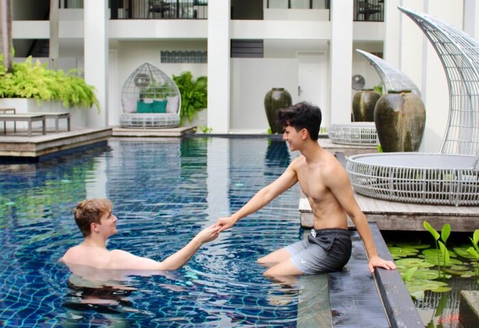 Gay couple at Outrigger Surin Beach Resort, Phuket. Honeymoon travel in Thailand. Top gay hotels. Man in pool holding hands. TikTok.
