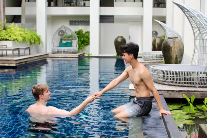 Gay couple at Outrigger Surin Beach Resort, Phuket. Honeymoon travel in Thailand. Top gay hotels. Man in pool holding hands. TikTok.