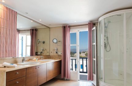 Poseidon Hotel Suites bathroom in Mykonos Town for gay honeymooners. Modern design with double sinks, shower, and balcony view. City Center.