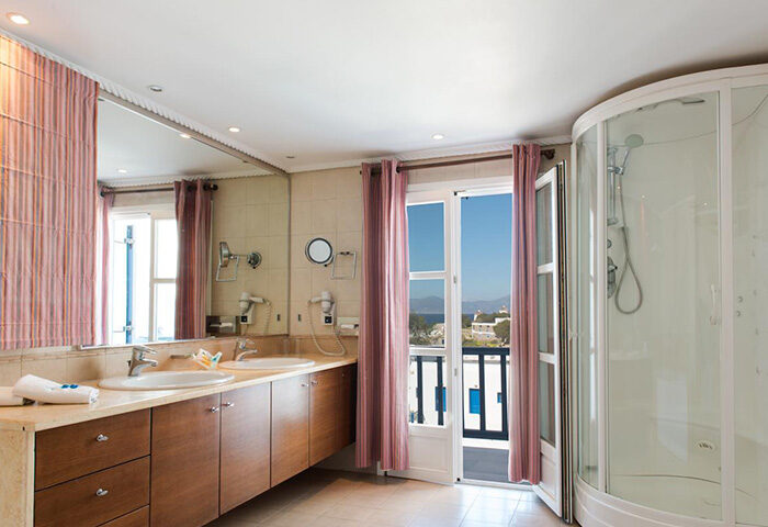 Poseidon Hotel Suites bathroom in Mykonos Town for gay honeymooners. Modern design with double sinks, shower, and balcony view. City Center.