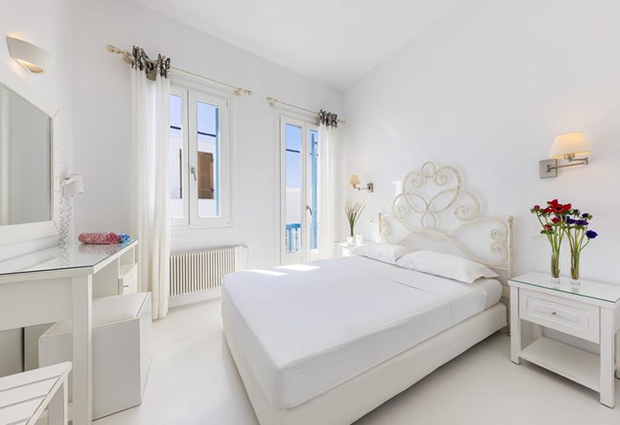 Carbonaki Hotel room, Mykonos. Honeymoon suite with white decor, double bed, and flowers. Ideal for gay couples in Mykonos Town, Chora.