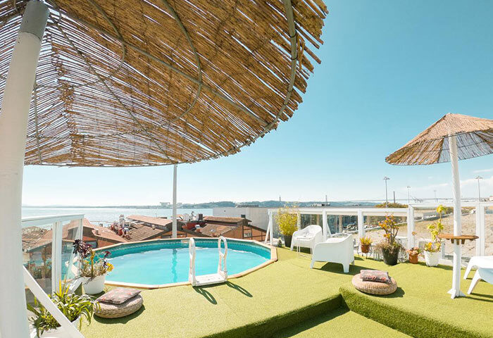 Sunset Destination Hostel rooftop pool. Lisbon gay beach hostel with pool, sun umbrellas, and ocean view. Top hostel for gay travel.