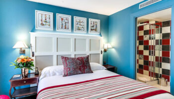 Les Tournelles Hotel room in Paris' Marais gayborhood. Blue walls, striped bedspread, and tiled shower. Instagram-able gay hotel.