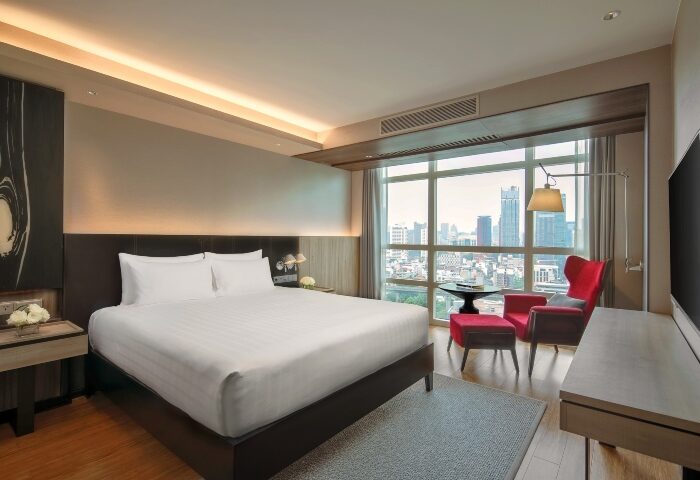 Pullman Bangkok King Power hotel room. Luxury gay honeymoon suite in Bangkok. City view, king bed, red chair. Top hotel for gay travel.