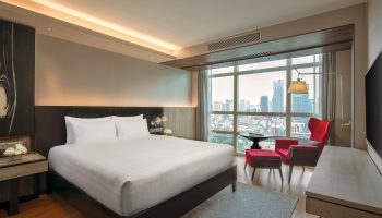 Pullman Bangkok King Power hotel room. Luxury gay honeymoon suite in Bangkok. City view, king bed, red chair. Top hotel for gay travel.