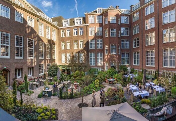 Sofitel Legend The Grand Amsterdam courtyard. Top luxury gay hotel on canal. Outdoor dining, lush gardens, and historic architecture.