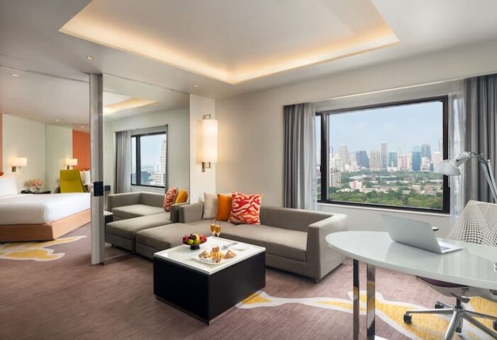 Crowne Plaza Bangkok Lumpini Park suite. Top luxury gay hotel room view, seating area, desk, and bedroom. Bangkok skyline visible.