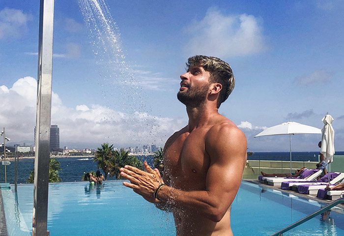 Gay travel: Man at W Barcelona beachfront hotel pool. Top luxury gay hotel in Barcelona. Enjoying the outdoor shower, beautiful view.