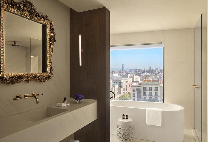 Luxury bathroom at The Barcelona EDITION, a top gay hotel. Features a soaking tub with a Barcelona city view, and ornate gold mirror.