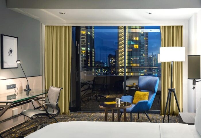 Voco Orchard Singapore hotel room at night. Luxury gay hotels Singapore. Balcony view of city lights. IHG Hotel room interior with desk and chair.