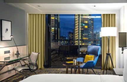 Voco Orchard Singapore hotel room at night. Luxury gay hotels Singapore. Balcony view of city lights. IHG Hotel room interior with desk and chair.