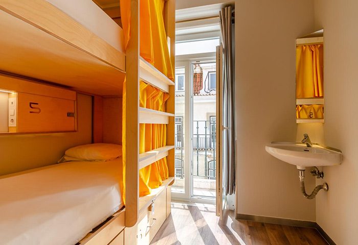 Lisbon Hostel dorm room with bunk beds, yellow curtains, sink, & balcony. Near Trombeta Bath gay sauna. Top party hostel for gay travelers.