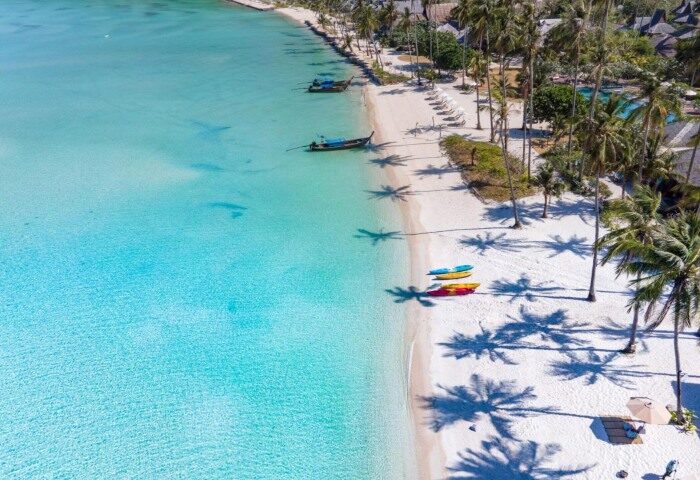 SAii Phi Phi Island Village's private beach. Aerial view of the white sand, turquoise water, palm trees, and boats. Gay travel destination.