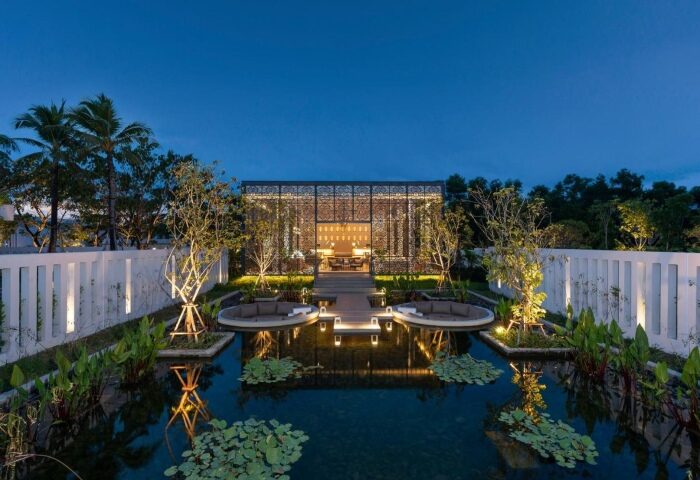 Melia Phuket Mai Khao romantic gay resort. A tranquil pond with lily pads reflects lights, leading to an elegant pavilion. Top gay Phuket resort.