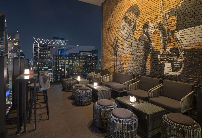 Hotel Indigo Bangkok Wireless Road's top rooftop gay bar. Features city views, mural, wicker furniture, and ambient lighting. Bangkok's nightlife.