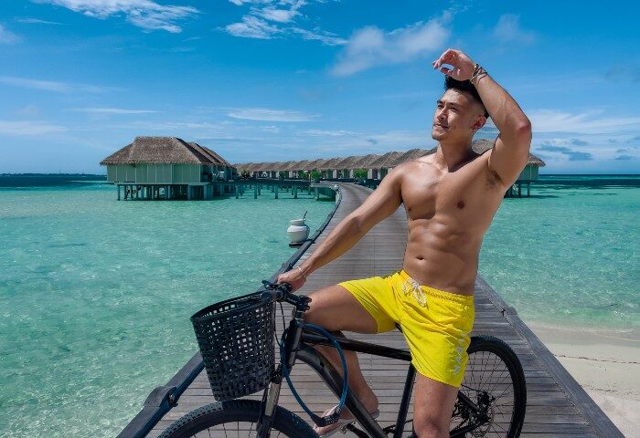 Gay travel: LUX* South Ari Atoll, Maldives. Man on bike, yellow shorts. Top staff friendly hotel, overwater bungalows. Paradise.
